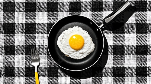 Obraz na płótnie Fried egg on a black pan, checkered tablecloth, sunny side up. w salonie