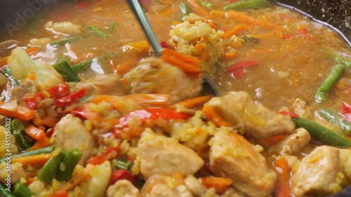 Bulgur with stewed meat and vegetables in sauce in a saucepan is stirred with a spoon. Close-up.