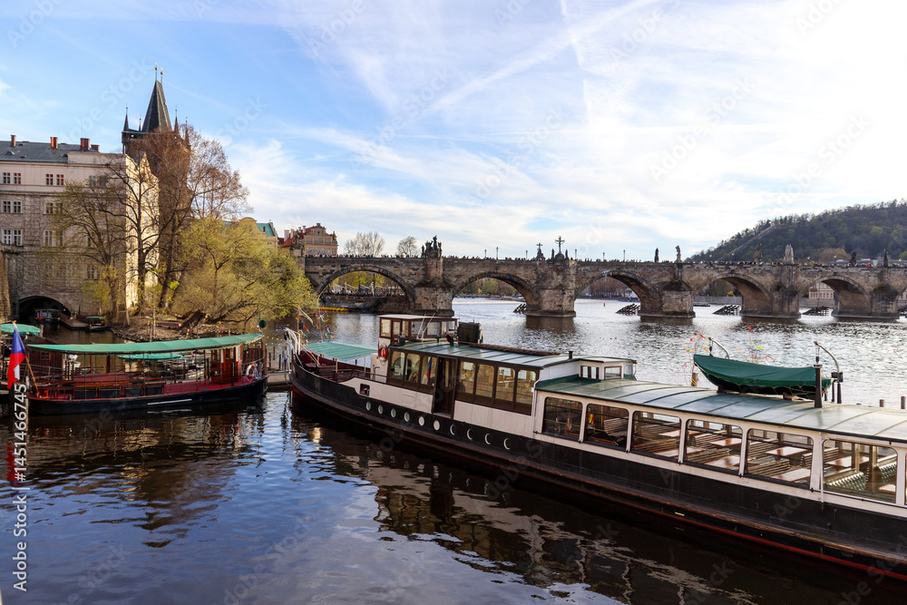 Fototapeta premium A picturesque cityscape with the Vltava River, Charles Bridge in the background and moored boats on the riverbank in Prague.