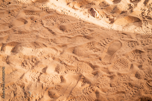 Multiple overlapping footprints and shoe treads pressed into the soft red sand of a desert trail, capturing the impact of foot traffic in a dry, sunlit landscape in the American Southwest