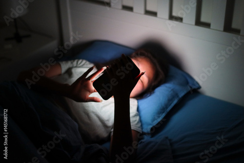 Young woman using smartphone in bed at night