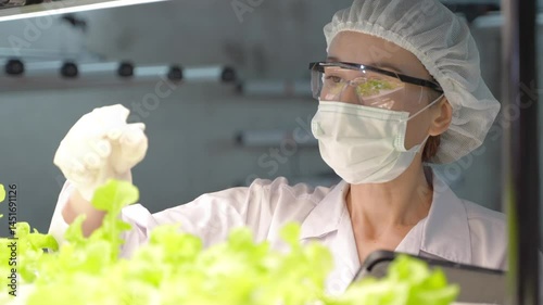 Scientist in protective gear testing hydroponic solution with microscope in indoor smart farming lab