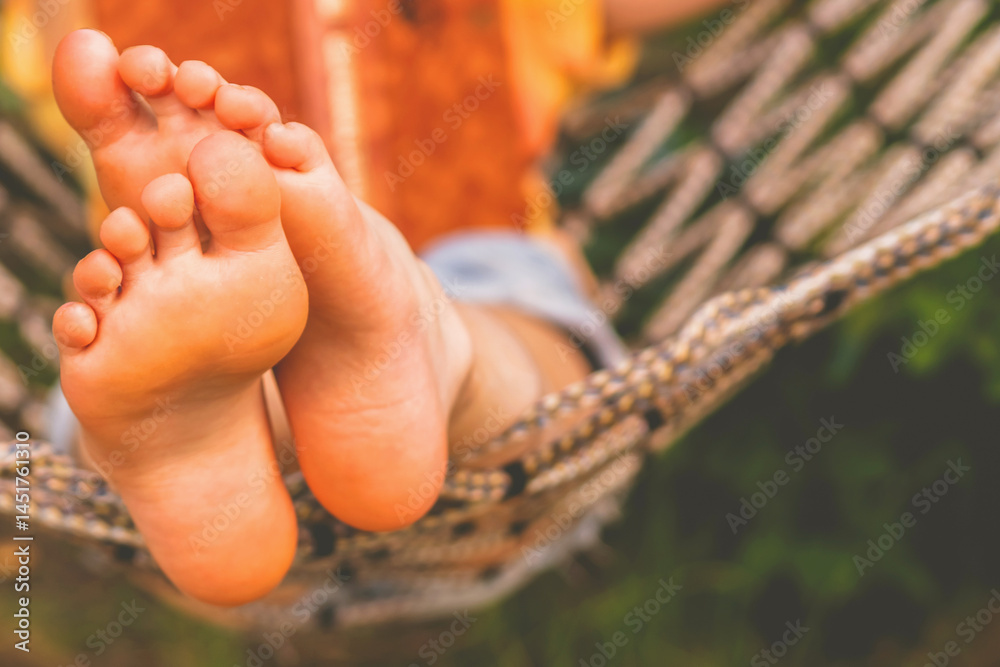 A young beautiful girl lies in a hammock and reads a book. Selective focus on feets. Horizontal image. Copy space for design.