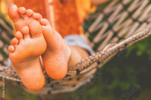 A young beautiful girl lies in a hammock and reads a book.  Selective focus on feets. Horizontal image. Copy space for design.