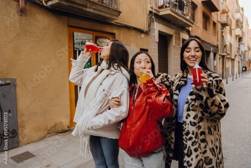 Wallpaper Mural A dark-haired, smiling Asian woman in her early 20s holding on to two dark-haired European female young friends, drinking juice while walking down the street. Torontodigital.ca