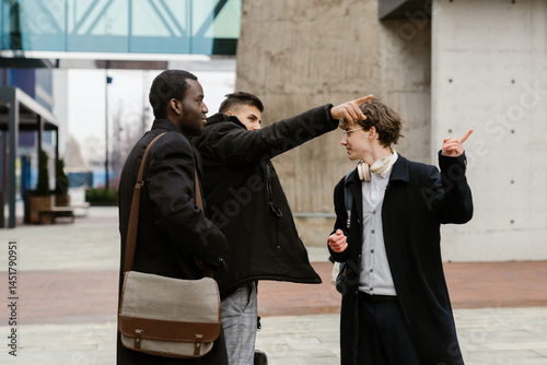Side view of a Black man in his early 30s looking at an adult European man pointing fingers with a European 30-year-old man together in the other direction and talking on the street in daytime.