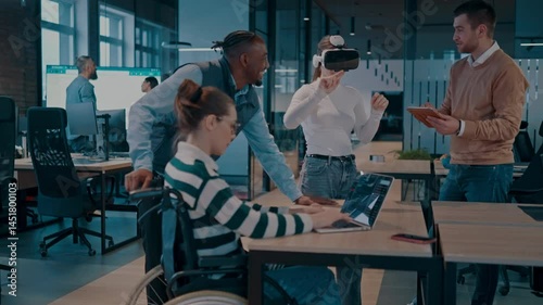Disabled businesswoman in a wheelchair working in modern coworking office. Team around is using virtual reality goggles, collaborating with the latest technology in an open space startup creative