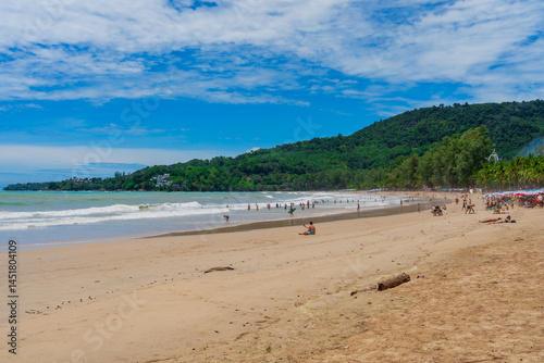 High-resolution resort scene: an orderly line of blue sun-loungers and emerald Chang umbrellas angles toward turquoise surf, backed by a stand of soaring coconut palms and a distant forested headland 
