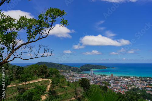 Ultra-sharp midday vista from a jungle ridge above Patong Bay, Thailand: emerald palms and terraced hills frame turquoise water, a cobalt sky with cotton clouds, and a cluster of modern towers and low