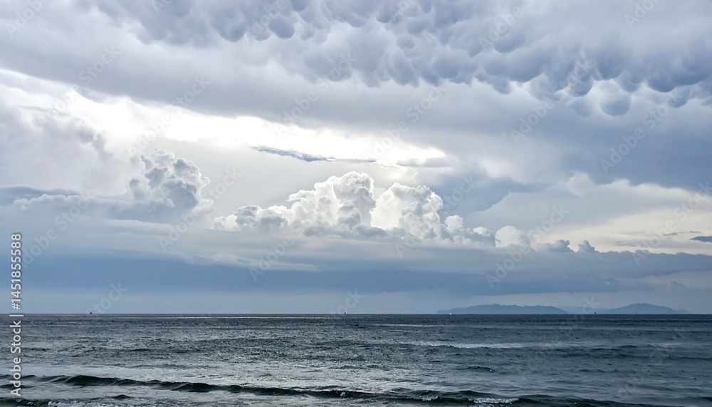 Obraz premium Dramatic seascape featuring turbulent, mammatus clouds over a tranquil ocean. Ideal for concepts of weather, natures power, or emotional landscapes.