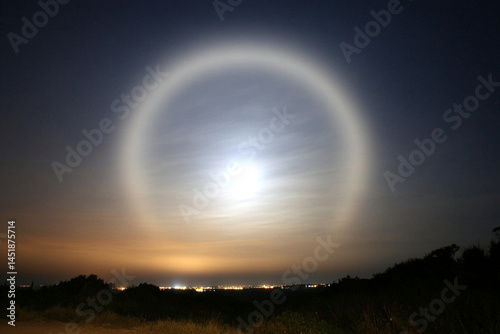 Moonbow creates a surreal arc of colors on a dark night over the distant city lights photo