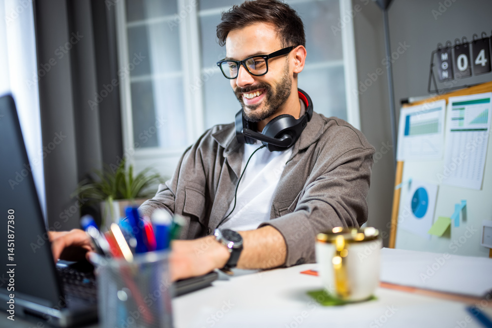 Fototapeta premium Young man working from home with headphones around his neck.