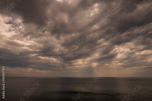 Sun between dark storm clouds over ocean. Dramatic seascape. Clouds and rain flurry over sea.