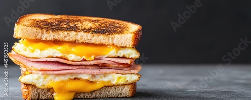 A toasted sandwich filled with ham, egg, and melted cheese sits on a dark background.