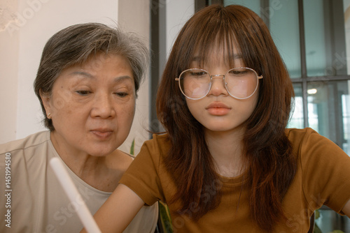 Fotografía Thai asian grandmother and teenage girl using tablet, nephew drawing or whiting while sitting on chair in cafe room, family spending time together