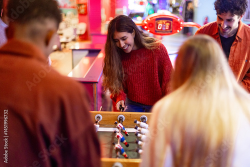 Friends playing foosball table soccer game in arcade