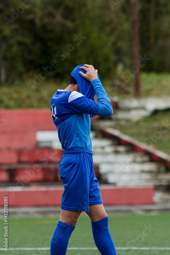 young soccer player in blue suit holds his head in his shirt in despair after losing the match