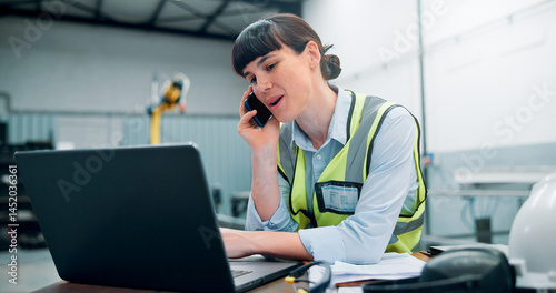 Engineer, laptop and phone call in robotics warehouse for manufacturing schedule, planning and project management. Woman, operator and tech in industrial factory for automation update with contact