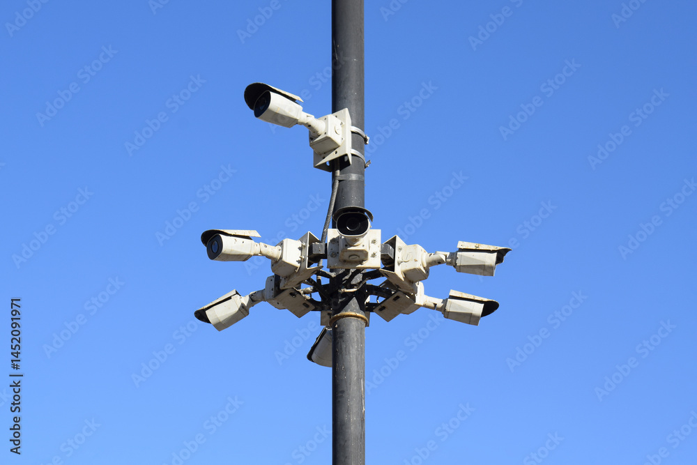 Several CCTV cameras mounted on poles with a blue sky background. Advanced security and surveillance at every corner Several CCTV cameras mounted on poles with a blue sky background. Advanced security and surveillance at every corner