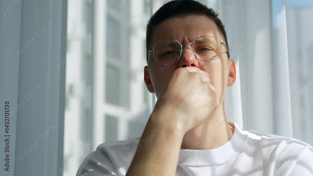 A man with poor eyesight in glasses sits in a bright room and thinks about something.
A dreamy guy at the window in sunny weather.
A man dreams and thinks about something