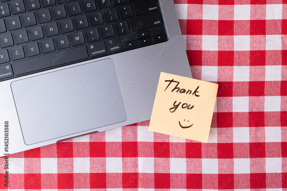 Obraz premium Remote workspace with laptop and Thank you note on red and white checkered table