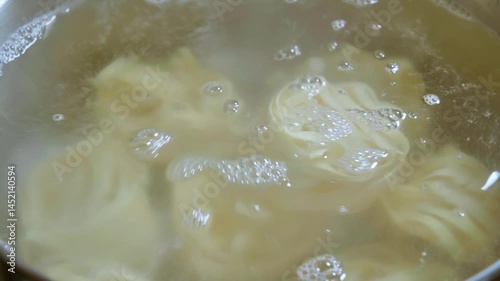 Close-up of a ball of tagliatelle pasta being placed in a pot of boiling water. Slow motion footage 100fps.