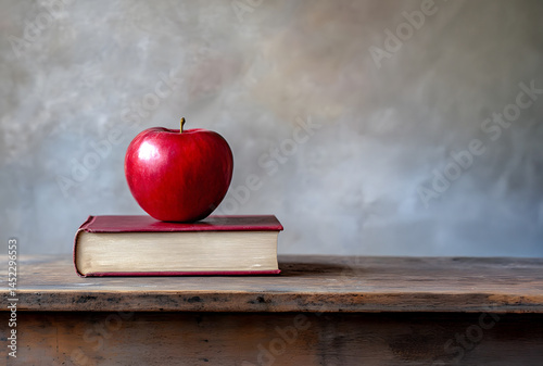 Obraz na płótnie Bright red apple resting on hardcover book atop rustic wooden table with soft neutral background, styled to highlight natural detail, balance, and calm indoor atmosphere with warm light. w salonie