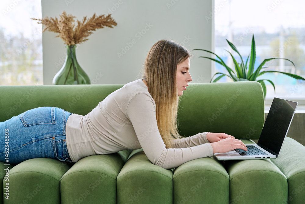 Young woman lying on sofa at home using laptop