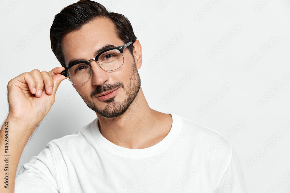 Fototapeta premium Young smiling man wearing glasses, casual white t-shirt, looking at the camera with a charming expression, isolated on solid light background. Stylish portrait concept.
