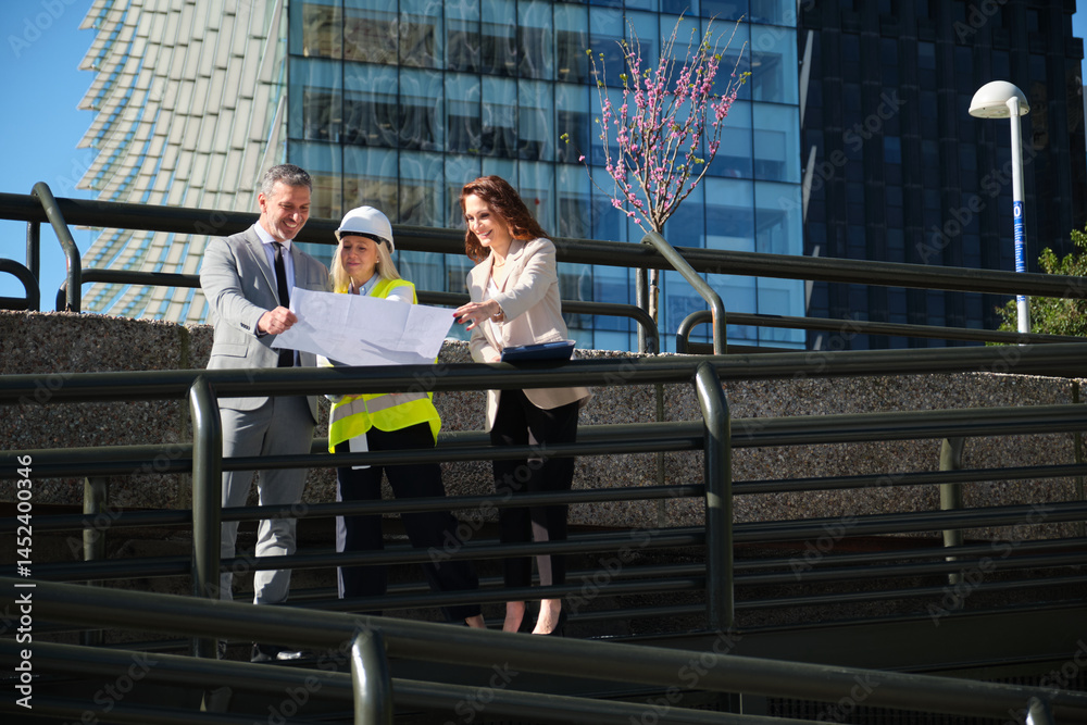 Architects and businesswoman reviewing blueprints outside modern building during a sunny day
