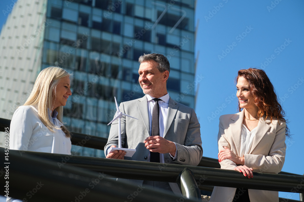 Business team discussing renewable energy project with miniature wind turbine in front of modern office buildings