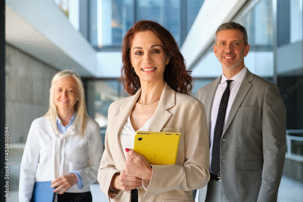 Business team smiling in modern office building holding tablet and documents