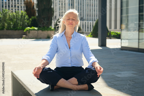 Obraz na płótnie Mature businesswoman practicing yoga in the city during her work break, finding peace and balance w salonie