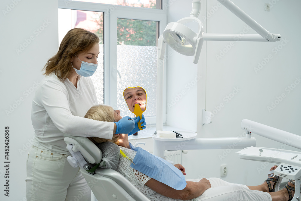 Fototapeta premium Senior female patient with dentist looks in the mirror and having dental treatment at dentist's office