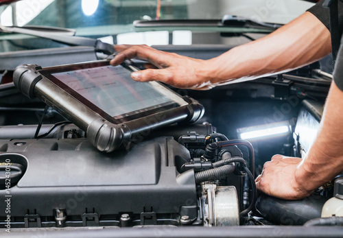 Car mechanic using tablet computer while examining engine