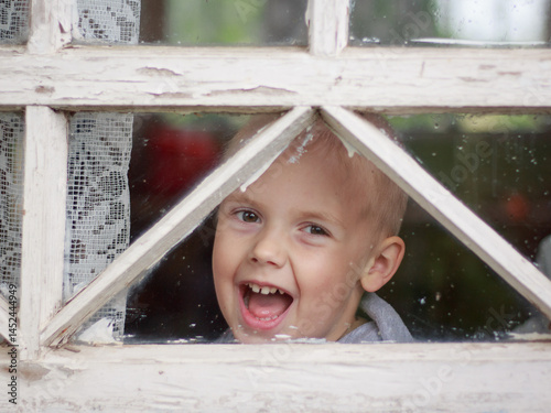 Child looking out through window in old wooden frame on veranda portrait, close-up, retro, rustic, vintage