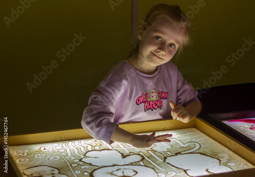  Beautiful little girl draws with sand on a light square, art therapy, sand animation, creative leisure for children, selective focus