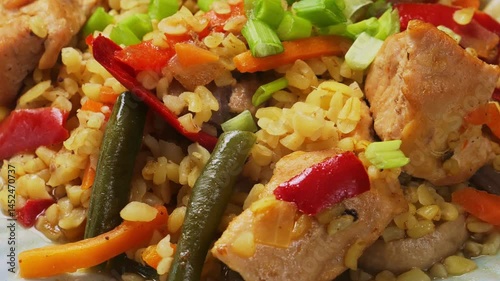 Bulgur with stewed meat and vegetables sprinkled with green onions rotating in a circle. Close-up.