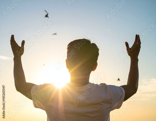 Man silhouetted against sunset, arms outstretched, birds in flight. A feeling of freedom and peace.