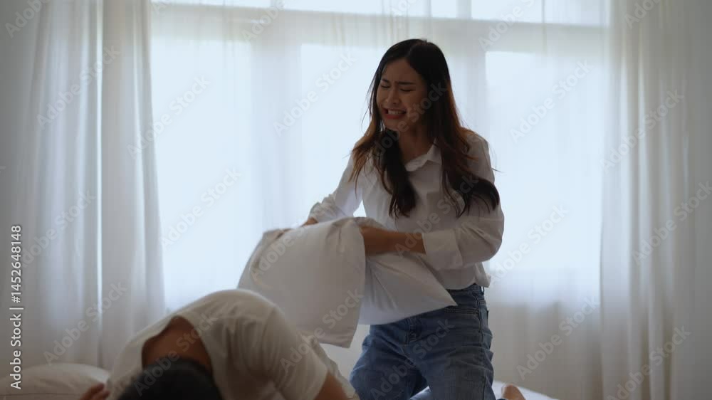 Cheerful young asian couple playfully wrestling with pillows, sharing intimate moment of joy and connection while laughing on bedroom bed during relaxed morning Cheerful young asian couple playfully wrestling with pillows, sharing intimate moment of joy and connection while laughing on bedroom bed during relaxed morning