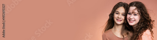 Obraz na płótnie Banner with studio portrait of two beautiful smiling sisters in peach and beige shirts against peach background w salonie