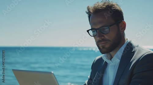 A good-looking businessman enjoys his summer break. He's working on his laptop by the sea. Even on vacation, he's getting things done and relaxing after work.
