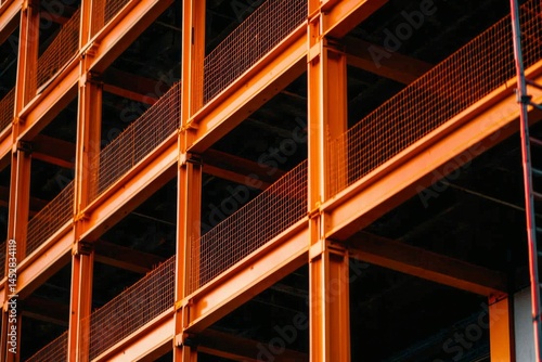 Metal framework of a building under construction with orange beams and black voids