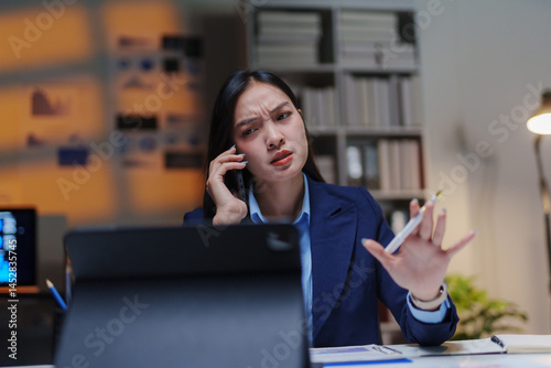 Young Asian businesswoman arguing on the phone while working late in the office, feeling overwhelmed by deadlines and pressure