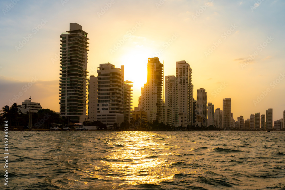 Fototapeta premium Sunset over the modern skyline of Cartagena, Colombia, seen from the sea with glowing reflections on the water and warm skies.