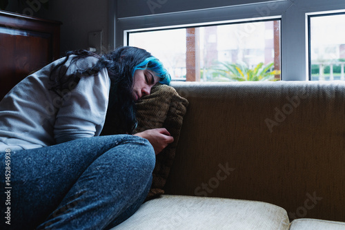 Sad woman with blue hair suffering from depression, lying on sofa at home