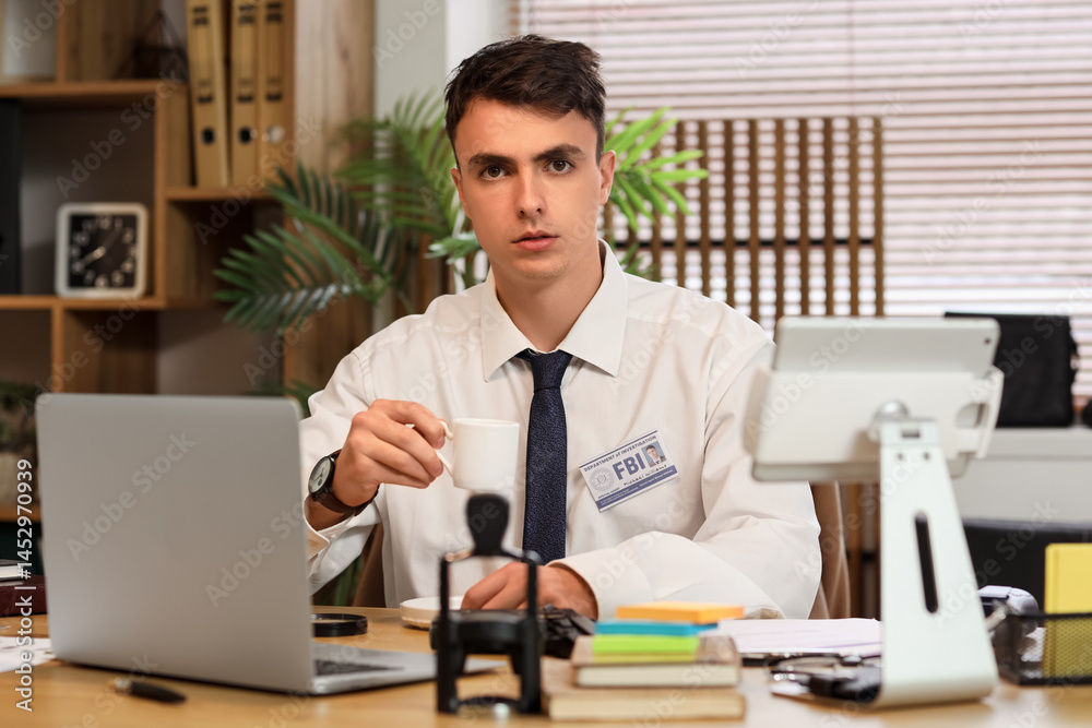 Fototapeta premium Male FBI agent drinking coffee at table in office
