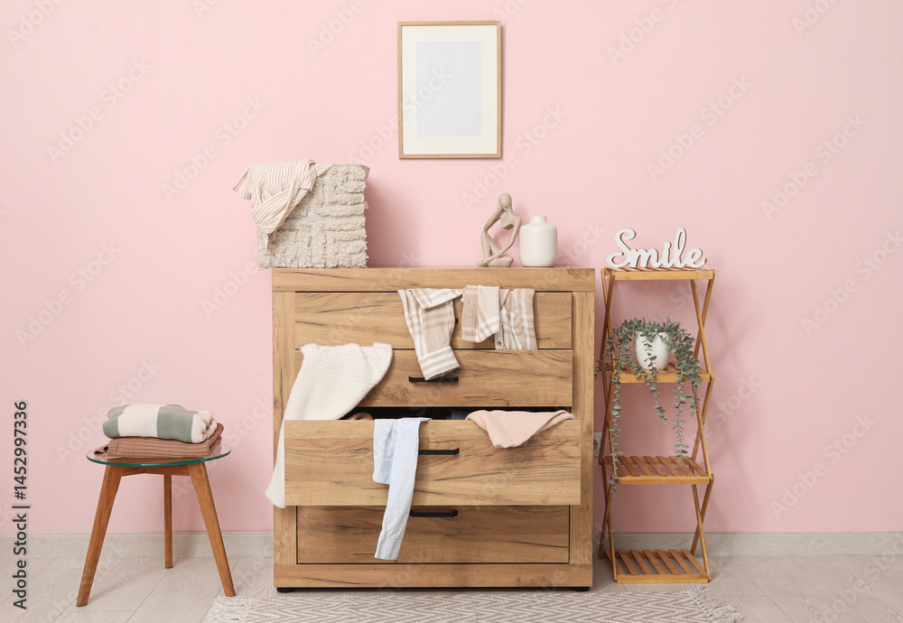 Obraz premium Shelving unit and commode with scattered clothes near pink wall in living room