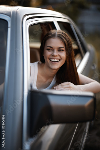 Cheerful young woman smiling from a car window, showcasing summer vibes and joy in a natural outdoor setting, perfect for lifestyle or travel concepts.