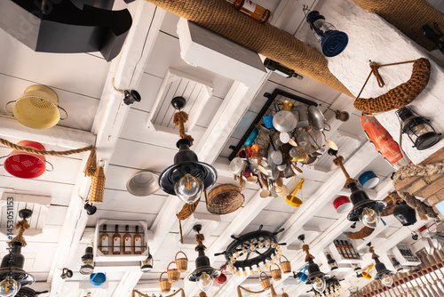 Eclectic ceiling decor in a Greek island restaurant with hanging lamps, baskets, and kitchen items.